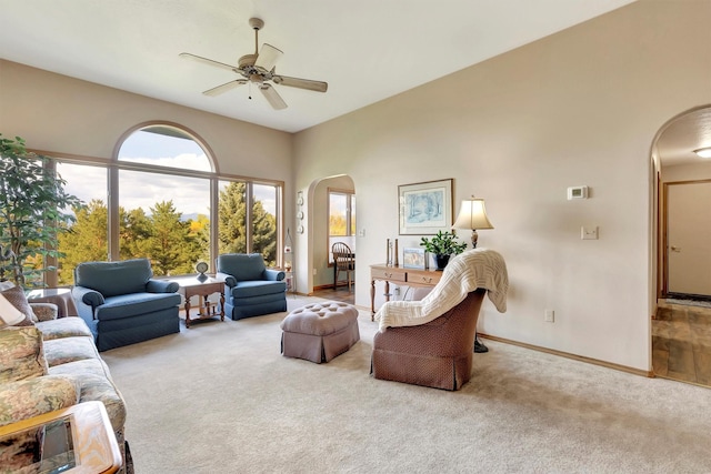 carpeted living room with arched walkways, baseboards, and a ceiling fan