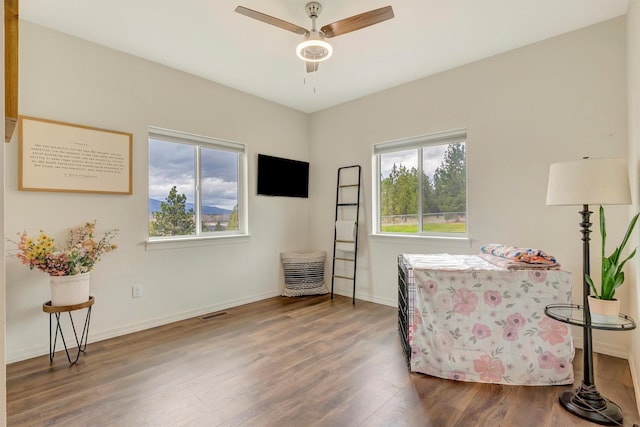 living area with baseboards, a ceiling fan, wood finished floors, and visible vents