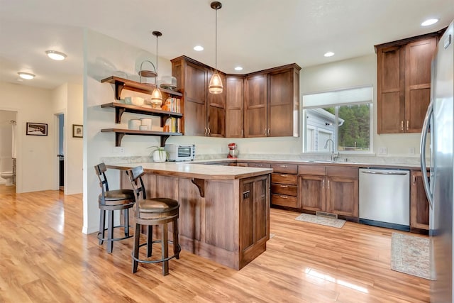 kitchen with open shelves, a peninsula, a sink, light wood finished floors, and appliances with stainless steel finishes