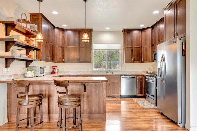 kitchen with light countertops, light wood-type flooring, stainless steel appliances, and a peninsula