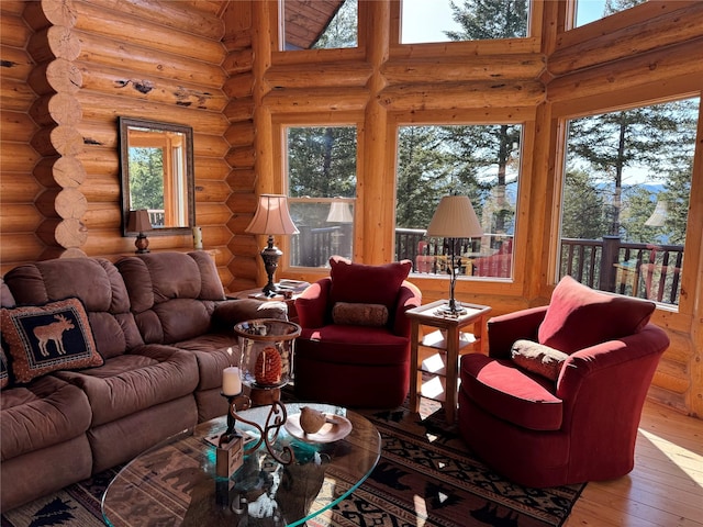 living room featuring log walls, a towering ceiling, a healthy amount of sunlight, and hardwood / wood-style flooring