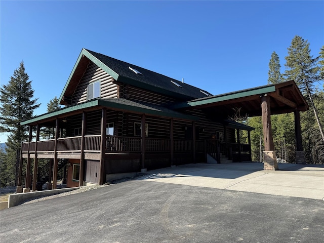 view of side of property featuring log exterior, a porch, driveway, stairway, and a carport
