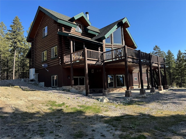rear view of property featuring a deck, log exterior, a patio, stairs, and stone siding