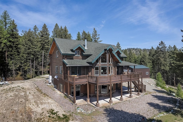 550 Jackson Meadows Rd, Kila, MT 59920 - back of house featuring log siding, a deck, a patio area, roof with shingles, and a wooded view