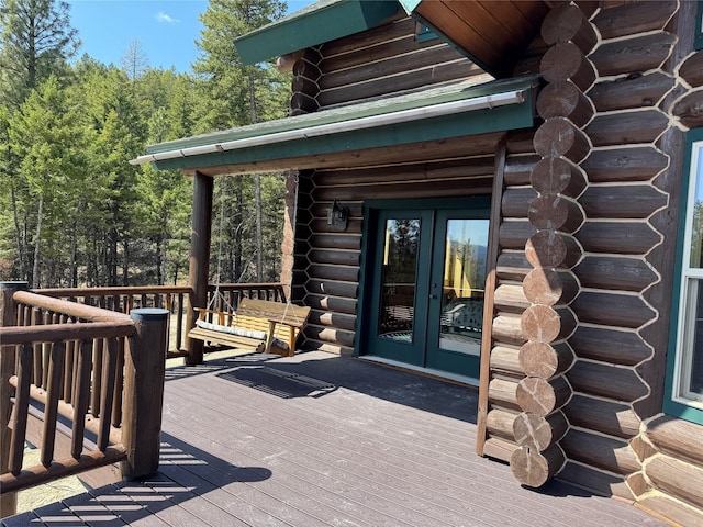 view of exterior entry with french doors, a deck, and log siding