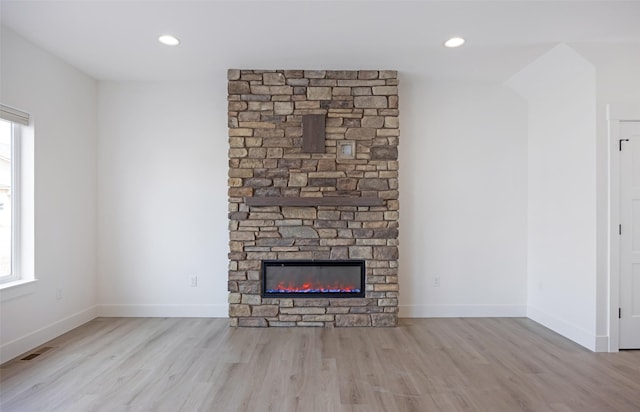 unfurnished living room featuring visible vents, a stone fireplace, a healthy amount of sunlight, and wood finished floors