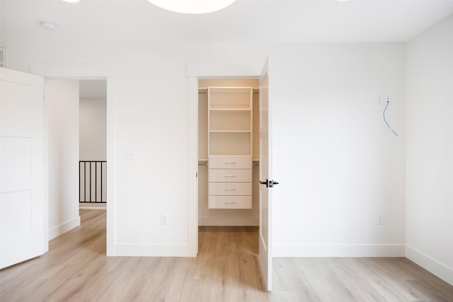 unfurnished bedroom with baseboards, a spacious closet, and light wood-style floors