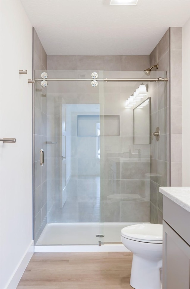 bathroom featuring toilet, a shower stall, wood finished floors, and vanity