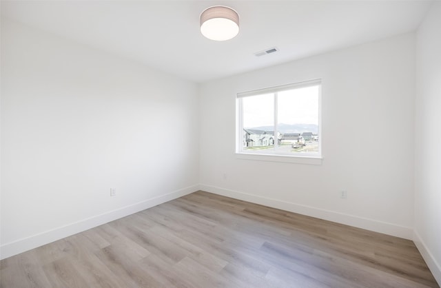 empty room with light wood-style floors, baseboards, and visible vents