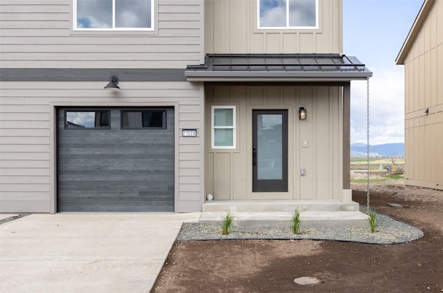 doorway to property with board and batten siding, a standing seam roof, metal roof, driveway, and an attached garage