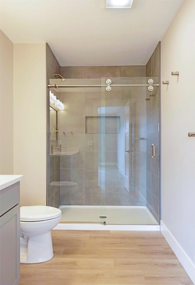 bathroom with toilet, a shower stall, wood finished floors, and vanity