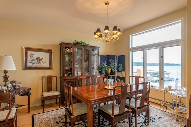 dining area featuring an inviting chandelier, a water view, baseboards, and light wood-style floors