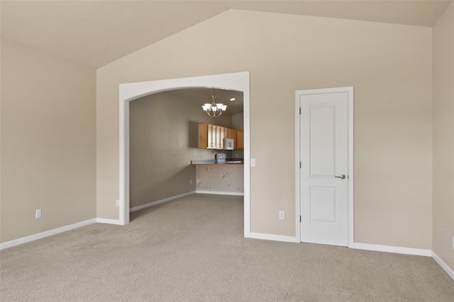 empty room with light colored carpet, baseboards, a chandelier, and vaulted ceiling