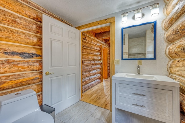 bathroom with vanity, toilet, a textured ceiling, and log walls