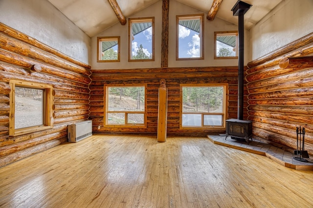 unfurnished living room with a wood stove, a healthy amount of sunlight, wood-type flooring, and high vaulted ceiling