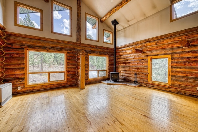 unfurnished living room featuring a wealth of natural light, a wood stove, log walls, and high vaulted ceiling