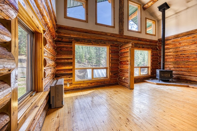 unfurnished living room featuring a wood stove, rustic walls, a healthy amount of sunlight, and high vaulted ceiling