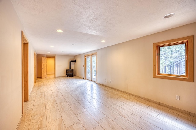 unfurnished room with baseboards, a wood stove, recessed lighting, and a textured ceiling