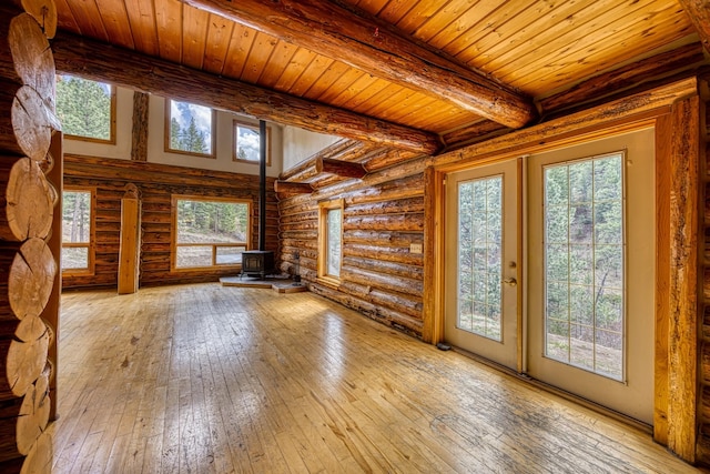 unfurnished living room featuring a wood stove, a healthy amount of sunlight, wooden ceiling, wood-type flooring, and beamed ceiling
