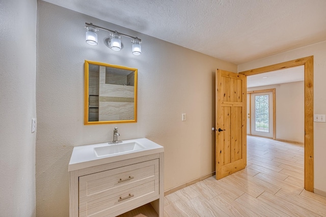 full bathroom with a textured ceiling, a shower, baseboards, and vanity
