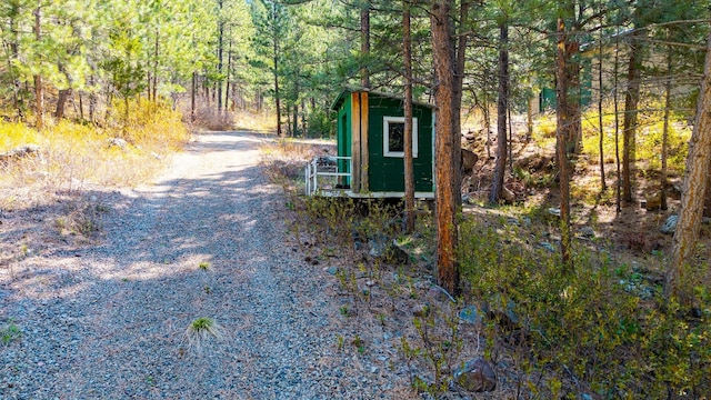 view of street with gravel driveway and a wooded view