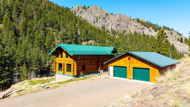 log-style house featuring a wooded view, a mountain view, log exterior, and an outbuilding