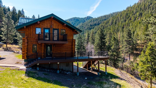 back of house with a wooded view, log siding, a deck with mountain view, and stairs