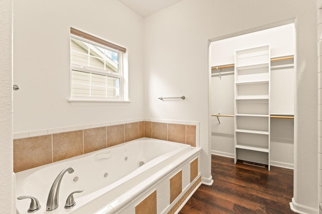 full bathroom featuring a jetted tub, a walk in closet, and wood finished floors