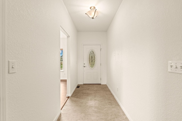 doorway to outside featuring baseboards, visible vents, and a textured wall