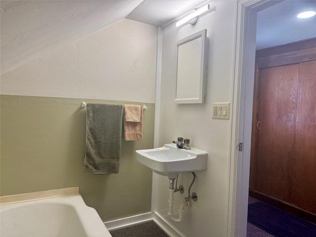 bathroom with a tub to relax in, baseboards, and lofted ceiling