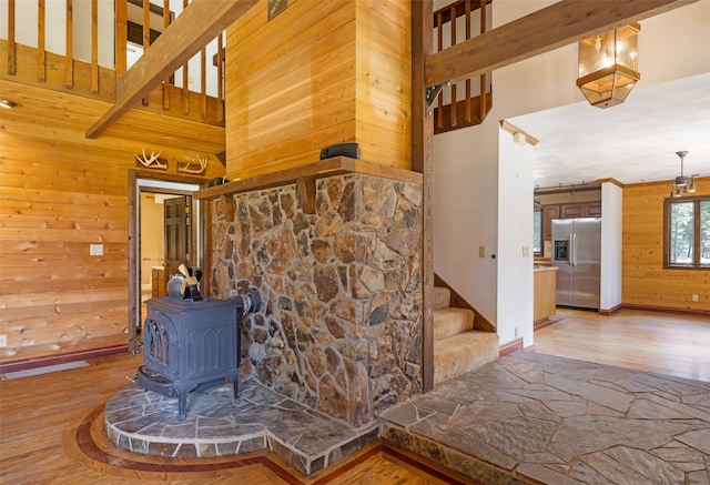 room details featuring wooden walls, stainless steel fridge, a wood stove, baseboards, and wood finished floors