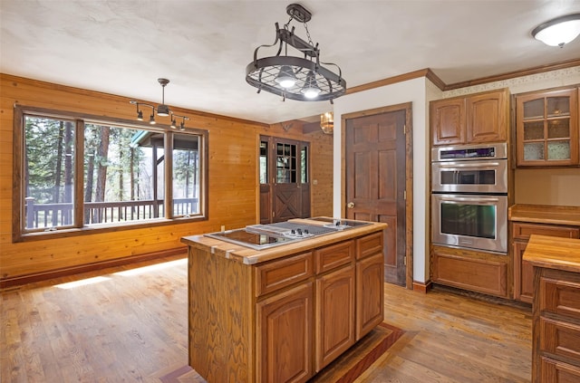 kitchen featuring stovetop with downdraft, stainless steel double oven, brown cabinets, wooden walls, and light wood-style flooring