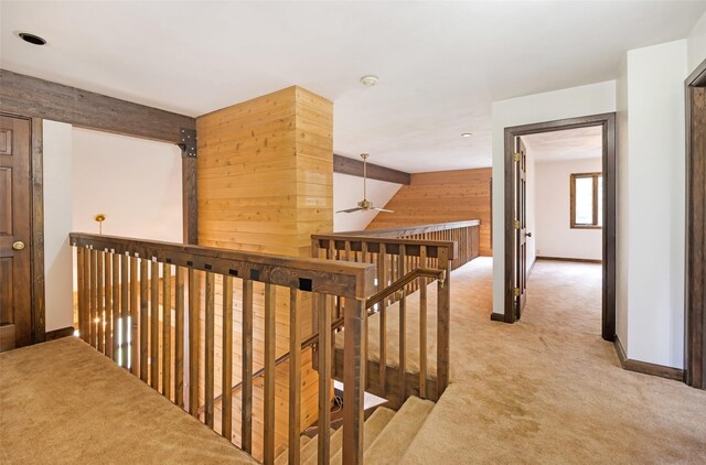 hall with light colored carpet, baseboards, wooden walls, and an upstairs landing