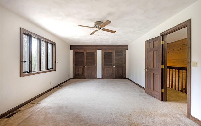 unfurnished bedroom featuring a ceiling fan, visible vents, baseboards, two closets, and light carpet