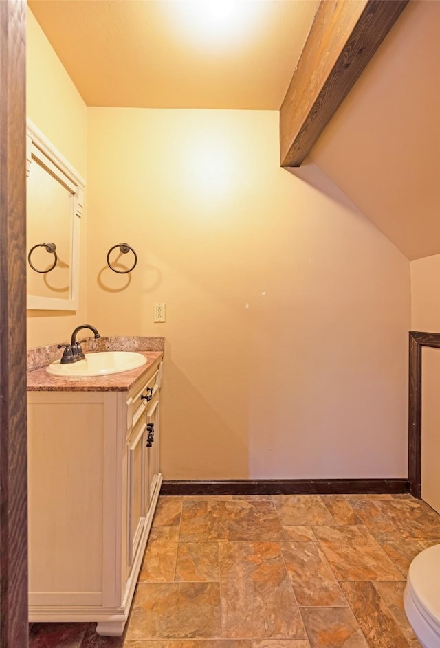 half bathroom with toilet, baseboards, stone finish floor, and vanity