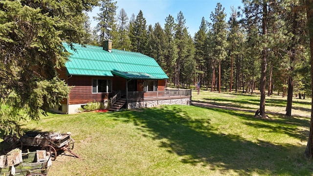 rear view of property featuring a standing seam roof, a view of trees, a chimney, a lawn, and metal roof
