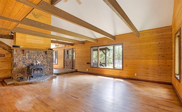 unfurnished living room with wood walls, lofted ceiling with beams, wood finished floors, and a wood stove