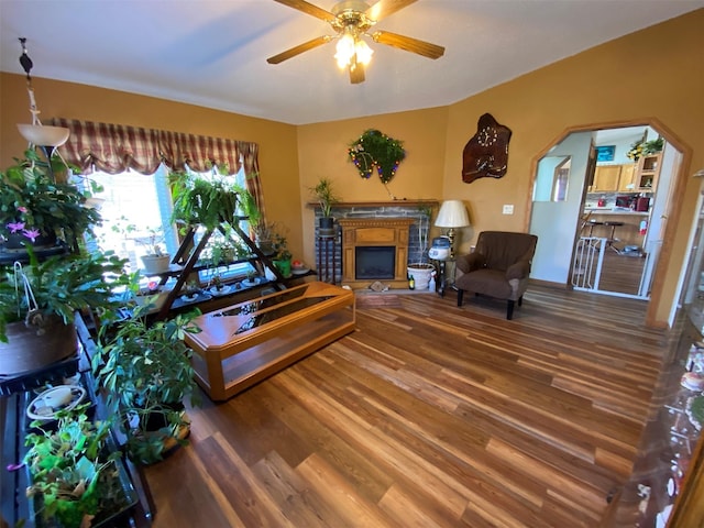 living room with arched walkways, ceiling fan, wood finished floors, and a fireplace