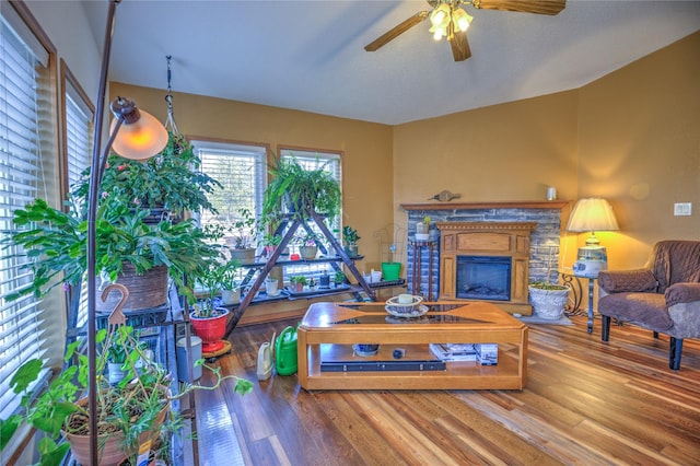 living area featuring a fireplace with raised hearth, a ceiling fan, and wood finished floors