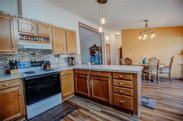 kitchen with range with electric cooktop, a peninsula, tile countertops, wood finished floors, and under cabinet range hood