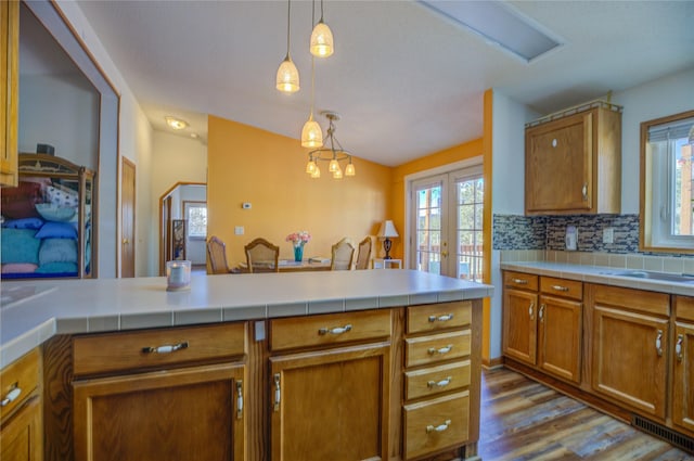 kitchen featuring dark wood-style flooring, brown cabinets, french doors, backsplash, and hanging light fixtures