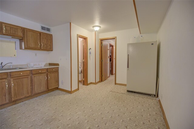 kitchen featuring freestanding refrigerator, visible vents, brown cabinetry, and a sink