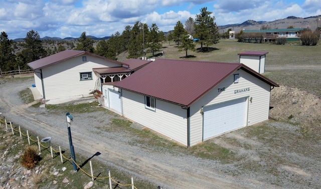 exterior space featuring a garage, dirt driveway, a mountain view, and metal roof