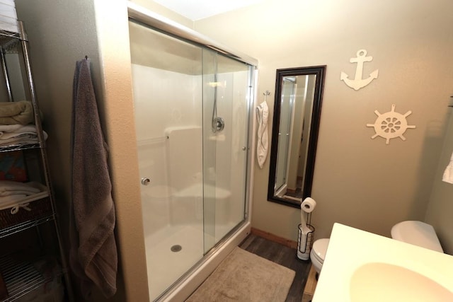 bathroom with a sink, a stall shower, toilet, and wood finished floors