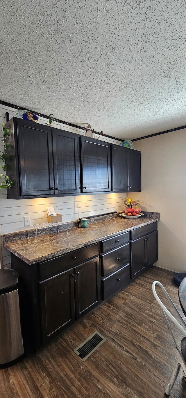 kitchen featuring a textured ceiling, visible vents, dark countertops, and dark wood finished floors