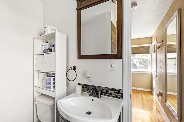 half bathroom with vanity, toilet, a textured ceiling, baseboards, and wood finished floors