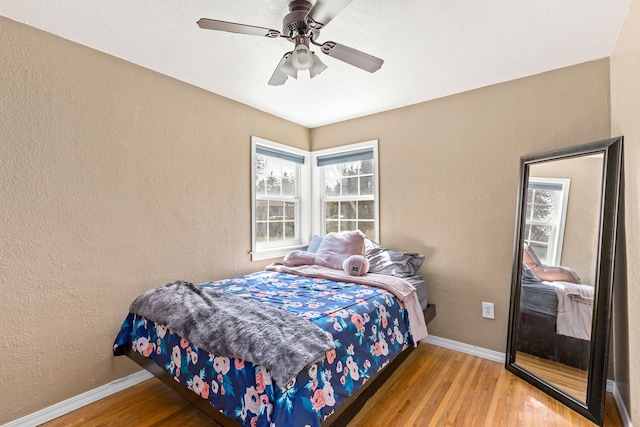 bedroom with baseboards, a textured wall, ceiling fan, and wood finished floors