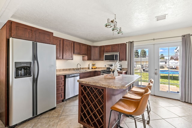 kitchen featuring light tile patterned flooring, a center island, a textured ceiling, french doors, and appliances with stainless steel finishes