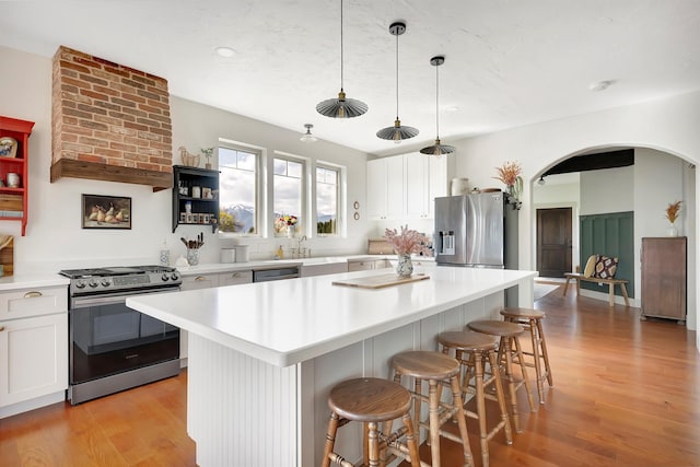 kitchen featuring appliances with stainless steel finishes, a breakfast bar area, arched walkways, light wood-style flooring, and a center island