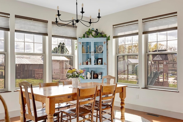 dining space with a chandelier, baseboards, visible vents, and wood finished floors